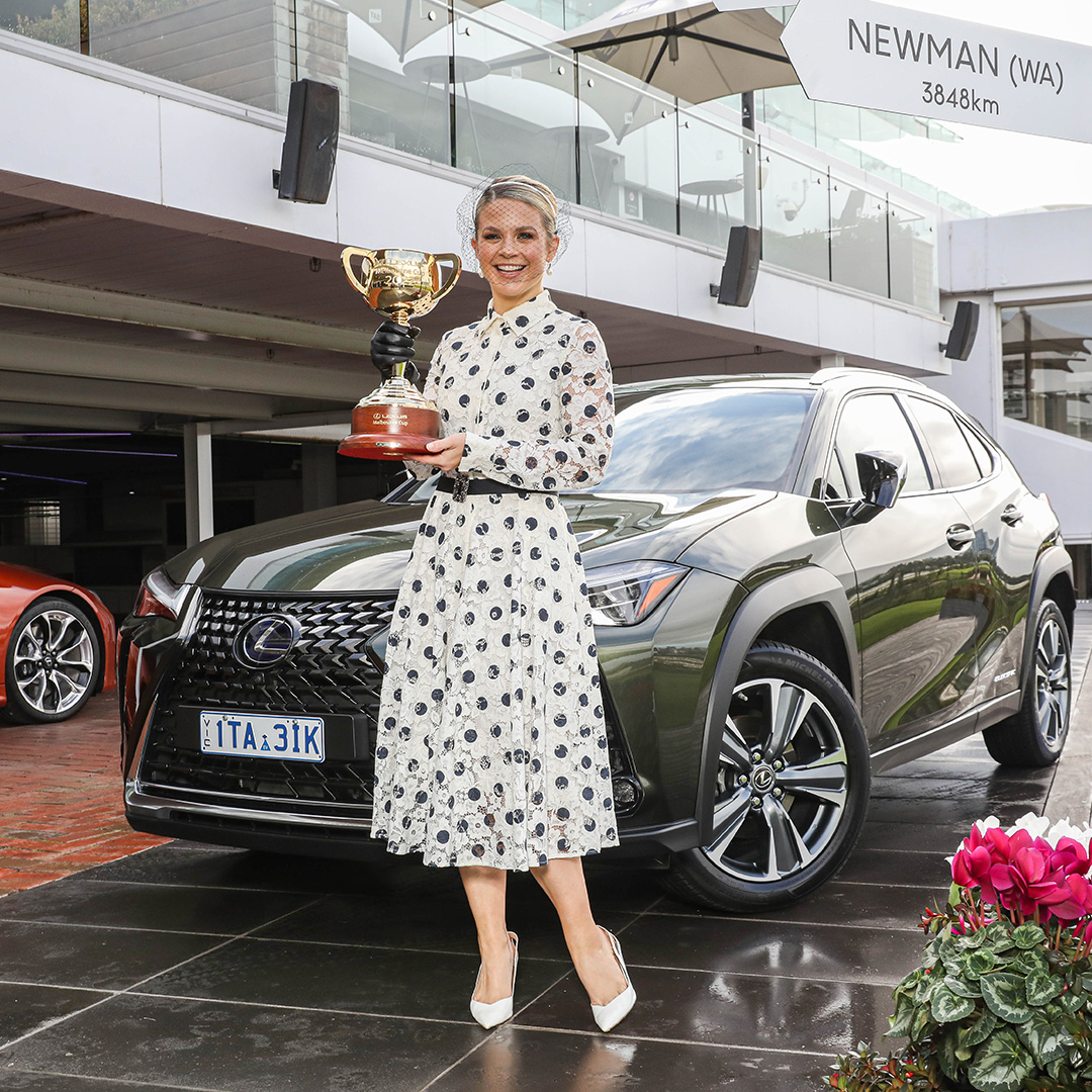 Emma Freedman holding the Lexus Melbourne Cup trophy and standing in front of a Lexus UX at Flemington racecourse