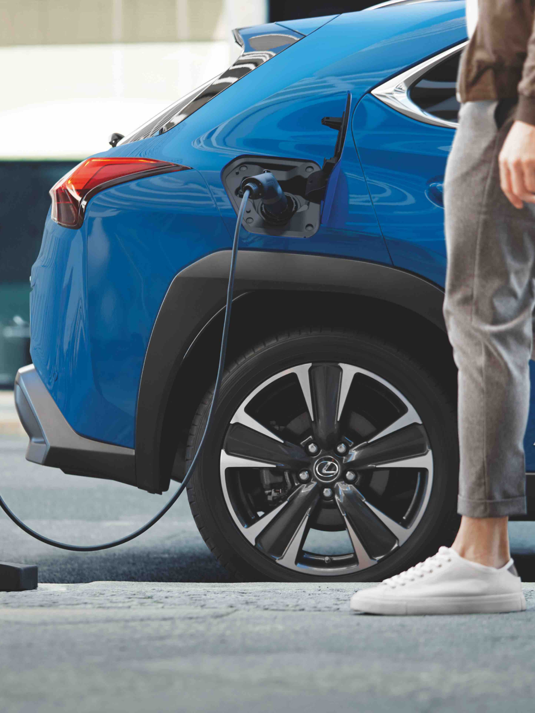 A blue UX 300e sits charging as someone walks past it.